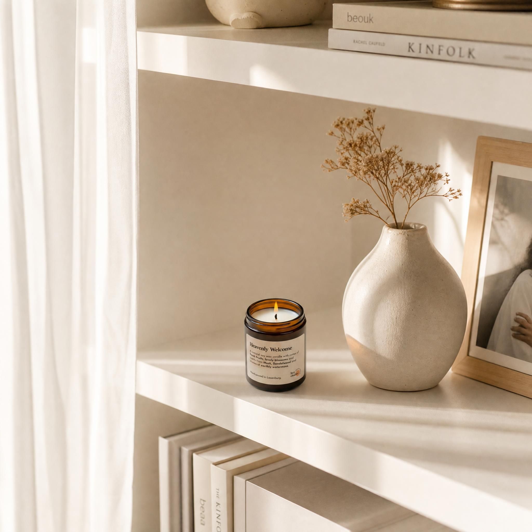 „Heavenly Welcome" Sojakerze auf hellem Bücherregal, weißes Interieur, florale Duftnoten – sanfte Eleganz für Zuhause