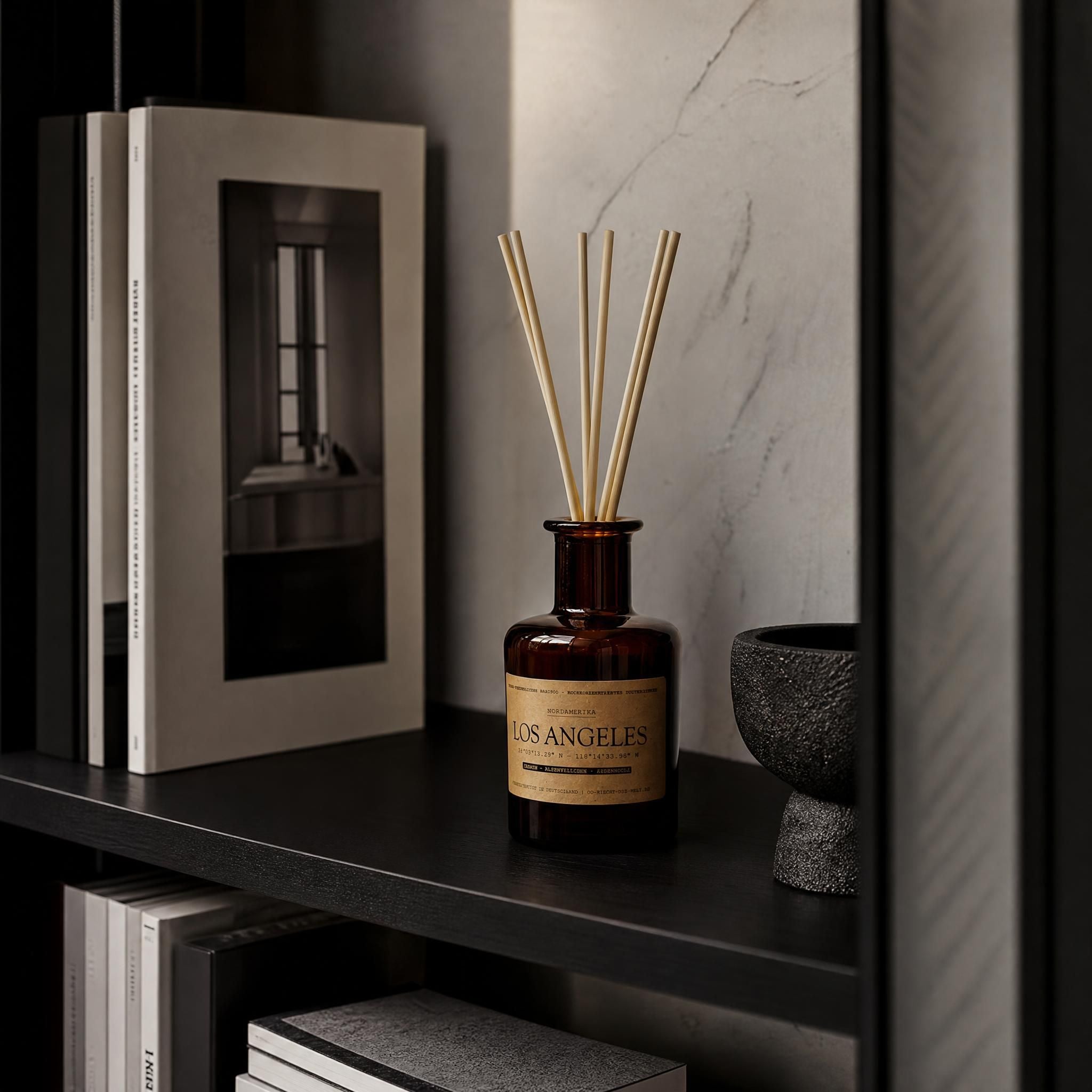 Diffuser „Los Angeles" Carrara-Marmor im Hintergrund, schwarzes Regal mit Architekturbuch und Marmor – Jasmin und Zedernholz